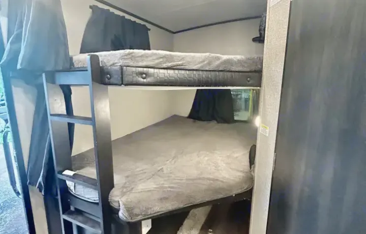 View of bunk beds in an RV rental, featuring dark frames and cozy grey bedding. Ideal for families and travelers.. Jayco White Hawk 2021