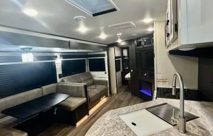 Modern RV rental interior: kitchen with sink, living space with seating, and a cozy fireplace.. Jayco White Hawk 2021