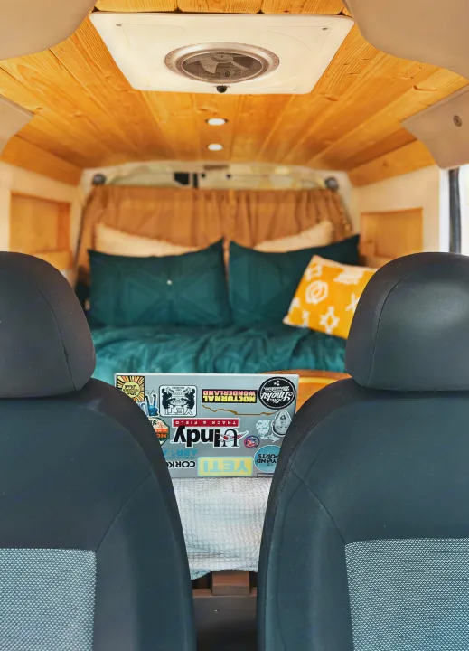 Cozy RV rental interior. View from front seats to bed with teal/yellow pillows. Wooden ceiling & laptop with stickers.. Dodge Dodge promaster city 2016