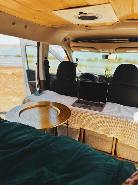 Enjoy remote work from this inviting rv rental. Van interior features a laptop, golden tray, and scenic water view.. Dodge Dodge promaster city 2016