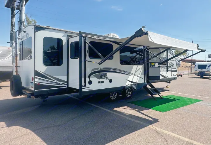 This modern travel trailer RV, perfect for your next rv rental, features an extended awning & outdoor steps. Sunny day on asphalt.. Jayco White Hawk 2020