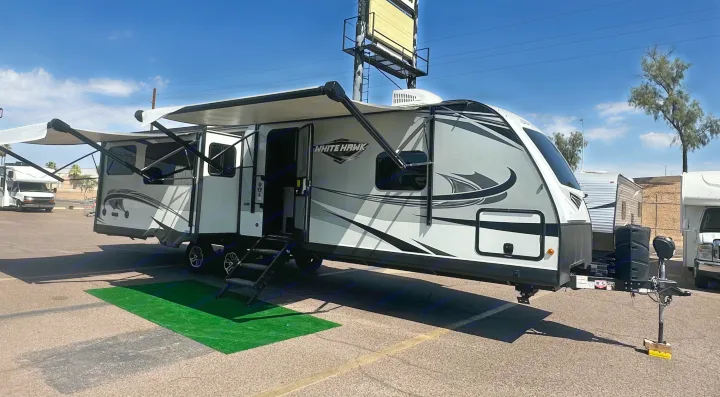 A sleek travel trailer, perfect as an RV rental, is displayed with awnings extended and steps down, ready for your next trip.. Jayco White Hawk 2020