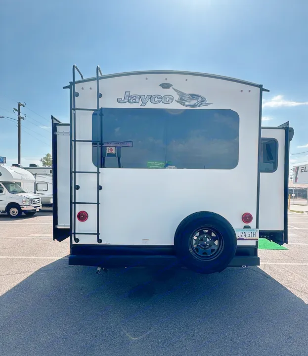 Back of a white Jayco RV rental, with a ladder, spare tire, and Arizona plate, parked on asphalt under a blue sky.. Jayco White Hawk 2020