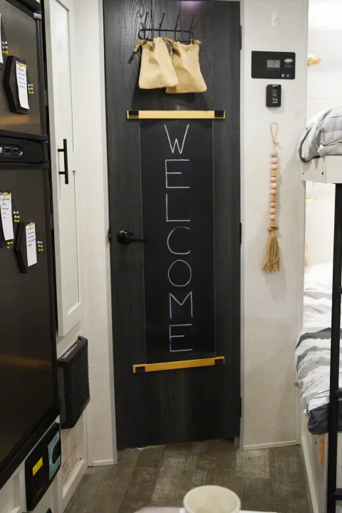 An inviting RV rental interior showing a "WELCOME" door, fridge with notes, bunk beds, and smart controls.. Forest River R-Pod 193 2022