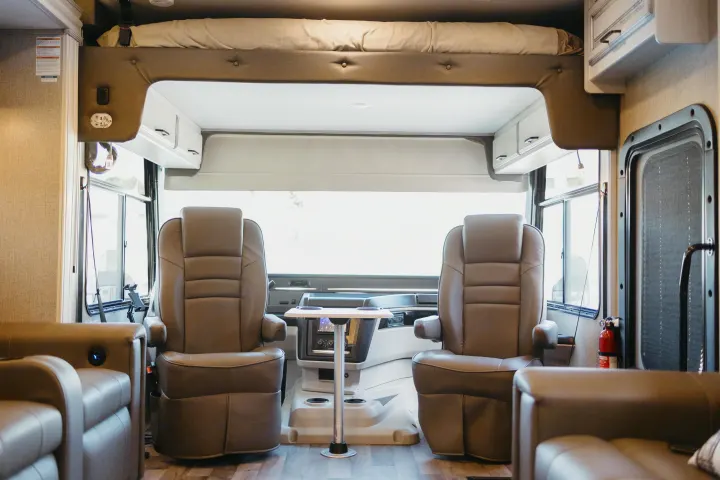 Spacious RV rental interior: cockpit with two brown seats, a small table, and a comfortable overhead bed.. Entegra Coach Vision XL 2021