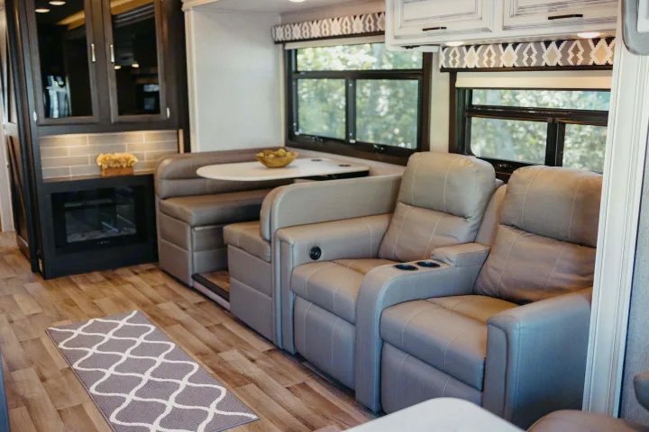 RV rental's inviting living area: gray theater seating, a comfortable dinette, and a cozy fireplace on wood flooring.. Entegra Coach Vision XL 2021