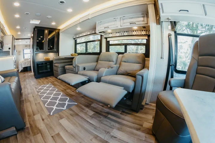 Spacious RV rental interior with recliners, dining booth, kitchen, and a peek into the bedroom area.. Entegra Coach Vision XL 2021
