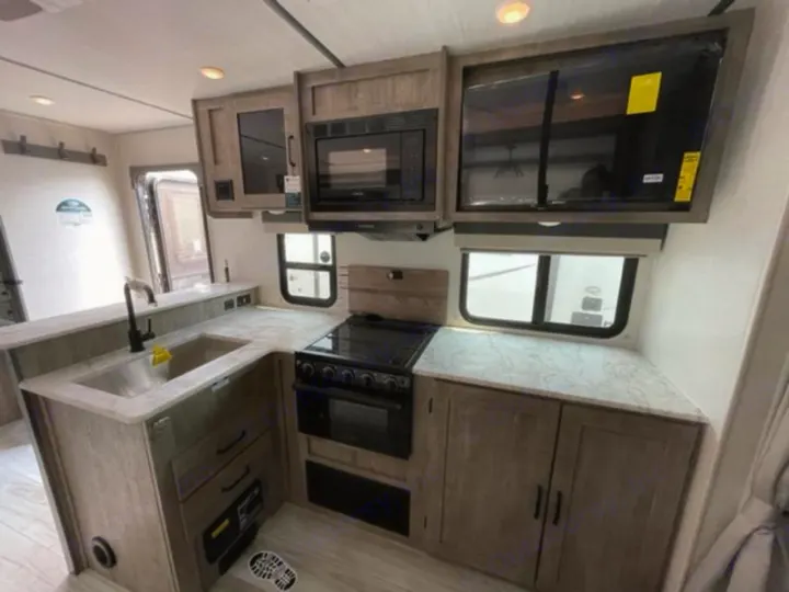 Explore this modern RV rental kitchen, featuring a full sink, stove, microwave, and TV setup for comfortable travel.. Forest River Surveyor Legend 2024