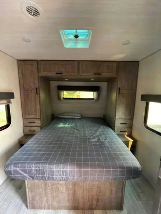 Inside an RV rental: a modern bedroom with a large bed, ample storage, skylight, and light wood finishes.. Forest River Surveyor Legend 2024