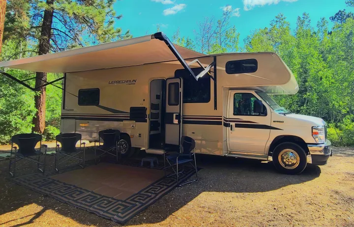 Coachmen Leprechaun RV rental: A Class C RV with an extended awning, outdoor rug, and chairs for a relaxing camp setup.. Coachman Leprechaun 2022