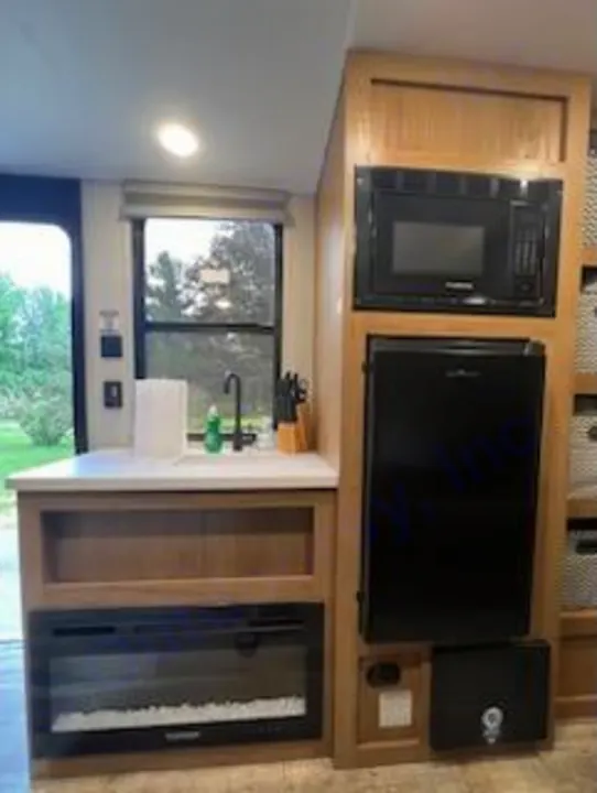 RV rental interior: a compact kitchen with sink, window, microwave, refrigerator, and an electric fireplace below the counter.. Forest River Cherokee 2024