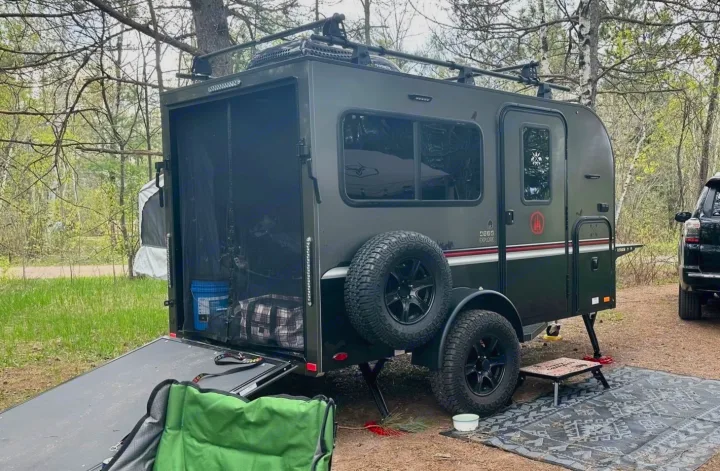 Off-road CEDA EXPLORE camper trailer RV rental with rear ramp down, set up for camping in a wooded outdoor site.. Intech Explore 2023