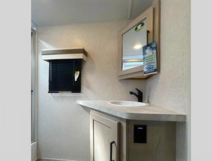 RV rental bathroom with light wood vanity, white sink, black faucet, mirror, and dark window blinds.. Forest River Rockwood Ultra Lite 2023