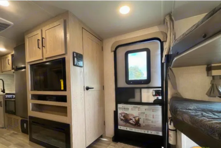 RV rental interior showcases a light wood finish, TV, fireplace, kitchen, bunk beds, and entry door for travel comfort.. Forest River Rockwood Ultra Lite 2023