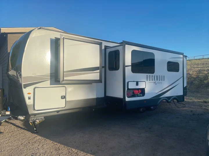 A white and gray Rockwood RV rental, with multiple slide-outs extended, parked outdoors on a sunny day.. Forest River Rockwood Ultra Lite 2023