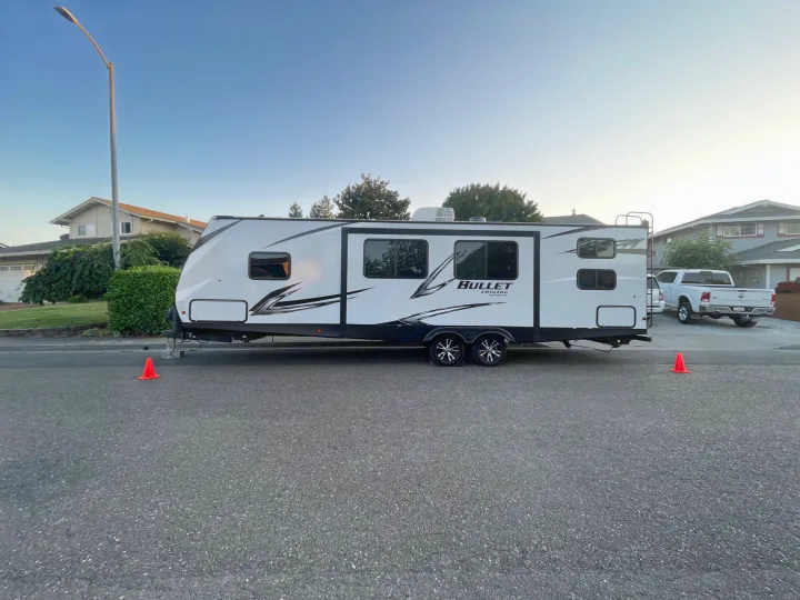 White Bullet Ultra Lite RV rental parked on a street with orange cones. Residential homes and trees are in the background.. Keystone RV Bullet Ultra Lite 2021