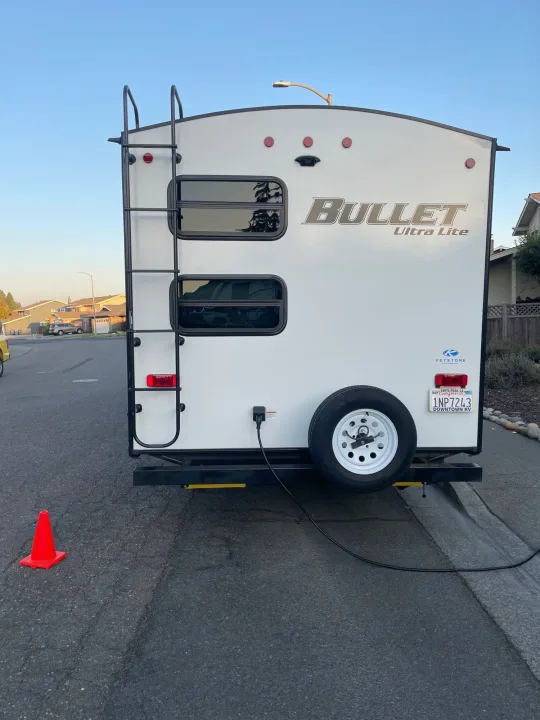 Rear view of a white "Bullet Ultra Lite" RV rental travel trailer, parked on a residential street. Features ladder & spare tire.. Keystone RV Bullet Ultra Lite 2021