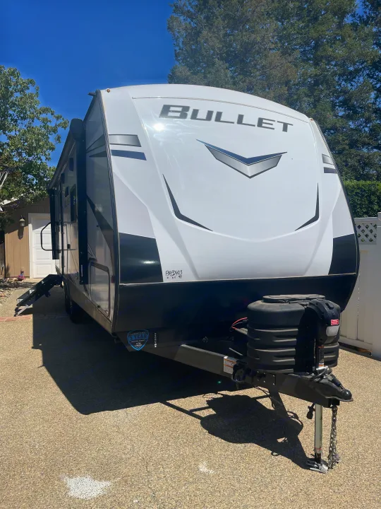 White & black Bullet travel trailer RV rental parked on pavement. Sunny outdoor scene.. Keystone RV Bullet Ultra Lite 2023