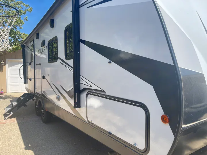 Side view of a bright, modern white & black travel trailer, perfect for an RV rental. Its inviting exterior and extended steps are ready for adventure.. Keystone RV Bullet Ultra Lite 2023
