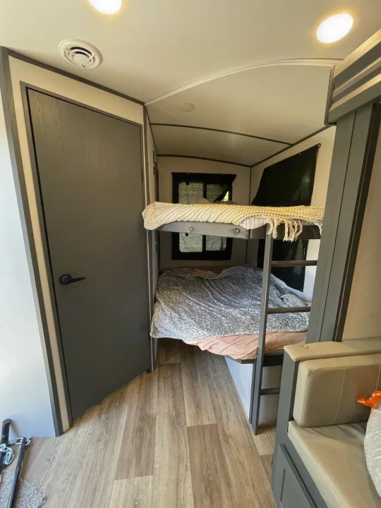 RV rental interior showing comfortable bunk beds, a door, and lounge seating, perfect for families.. Keystone RV Bullet Ultra Lite 2023