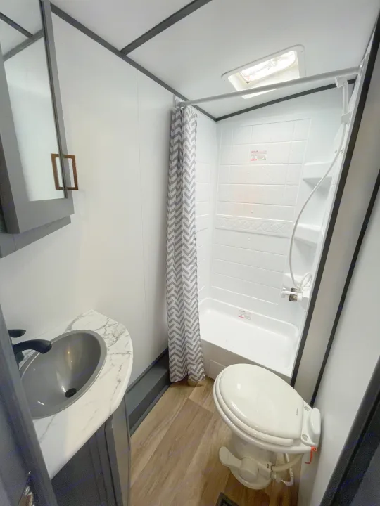 RV rental bathroom: Features include a white shower with skylight, toilet, and stylish sink vanity.. Keystone RV Bullet Ultra Lite 2023