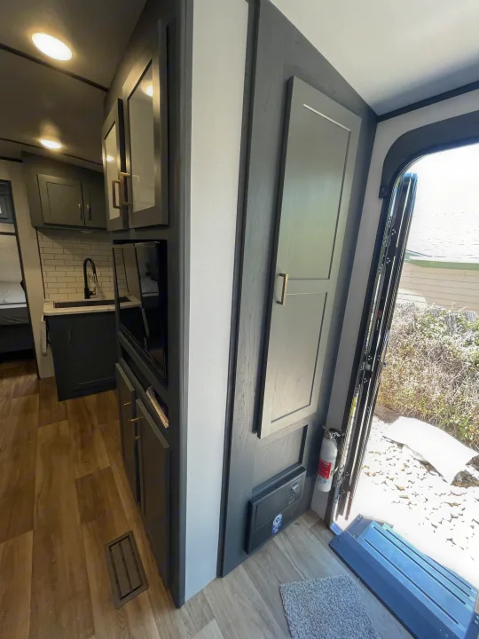 RV rental: Modern kitchen with dark cabinets, subway tile backsplash, wood floor & fire extinguisher by the open door.. Keystone RV Bullet Ultra Lite 2023