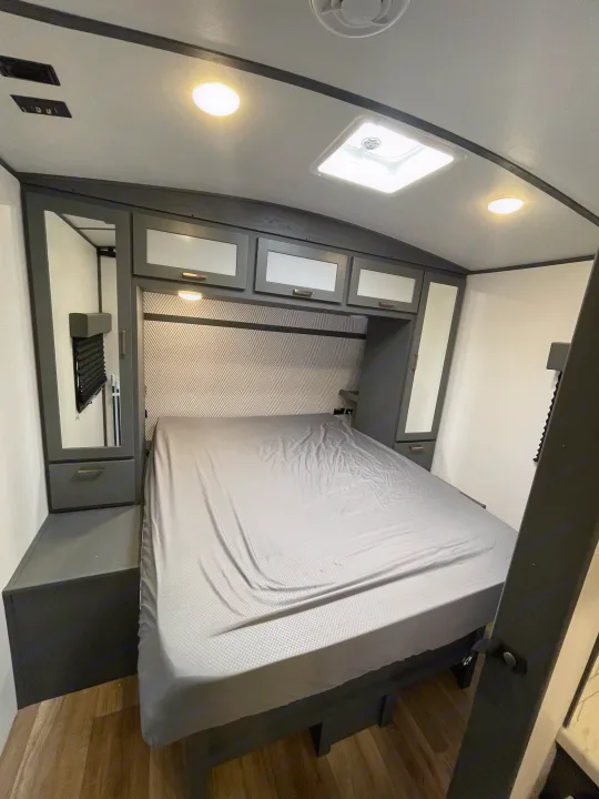 Modern grey RV rental bedroom featuring a comfortable bed, integrated storage, and bright overhead lights.. Keystone RV Bullet Ultra Lite 2023
