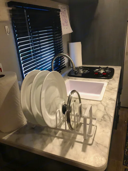 RV rental kitchen counter featuring a sink, two-burner stove, paper towel roll, and a dish drying rack with plates.. Aspen Trail 17BH 2021