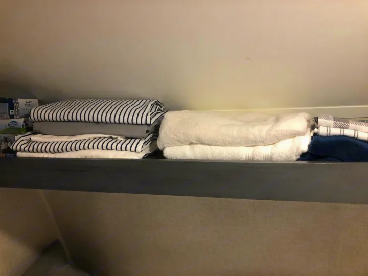 Neatly stacked bedding, towels, and linens are organized on a shelf inside an RV rental.. Aspen Trail 17BH 2021