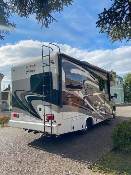 This spacious Solera Class C RV rental, with distinct graphics, is parked on an asphalt lot under a bright blue sky.. Solera Solera Motorhome 2014