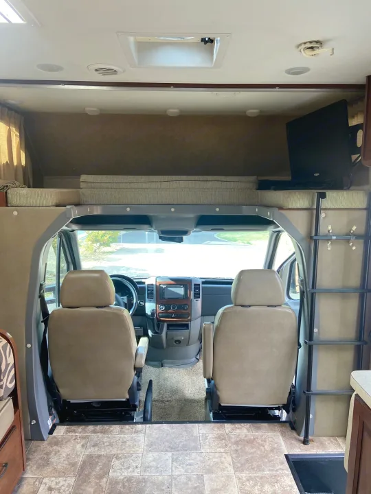 Inside this RV rental, a view of the front cockpit with driver and passenger seats, plus an overhead bunk and ladder.. Solera Solera Motorhome 2014