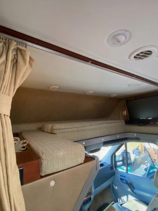 RV rental interior: A cozy overhead bunk bed with cushions, built-in TV, and view into the front cabin.. Solera Solera Motorhome 2014
