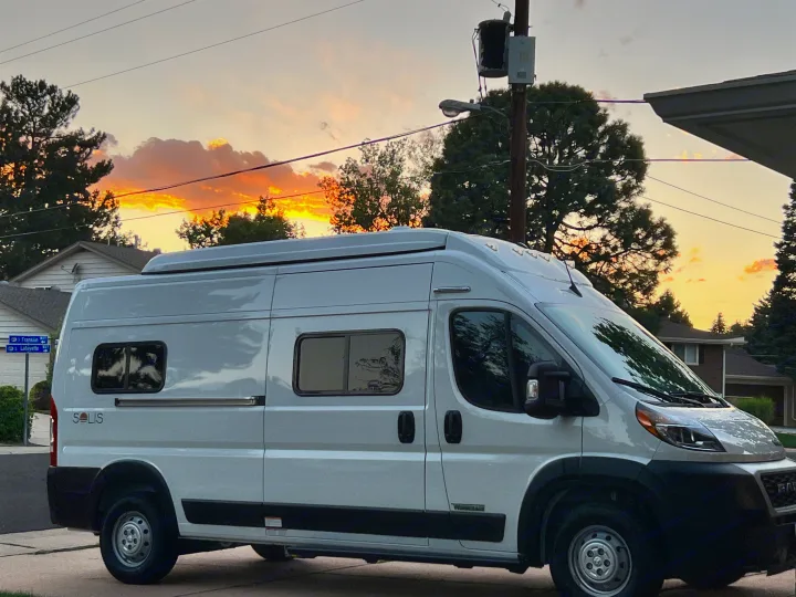 White Winnebago Solis, a camper van suitable for an RV rental, parked on a street at sunset with vibrant orange clouds.. Winnebago Solis 2023