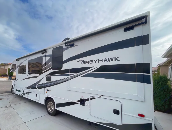 A large white Jayco Greyhawk RV, adorned with black and grey graphics, is parked, perfect for your next rv rental.. Jayco Greyhawk 2022