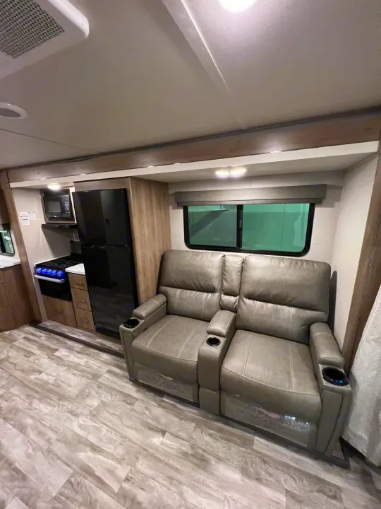 Comfortable RV rental interior featuring gray recliners, a compact kitchen with fridge and stove, and wood-look flooring.. Grand Design Imagine 2023