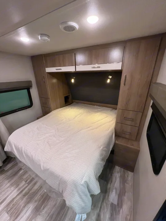 Bright RV rental bedroom with comfy bed, overhead storage, reading lights, & window.. Grand Design Imagine 2023