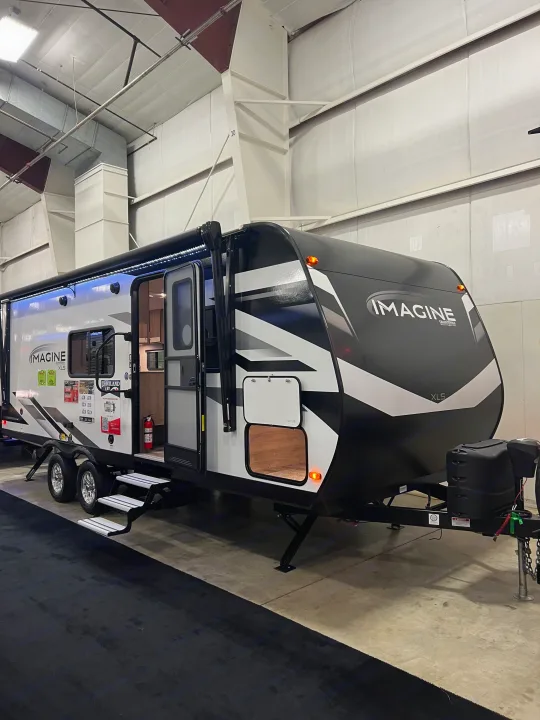 Explore this Imagine XLS travel trailer, an ideal rv rental option. It features a deployed awning with LED lights and open entry steps, shown indoors.. Grand Design Imagine 2023