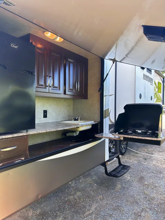 RV rental outdoor kitchen setup with refrigerator, sink, and stove. Perfect for camping adventures!. Keystone RV Montana Mountaineer 2015