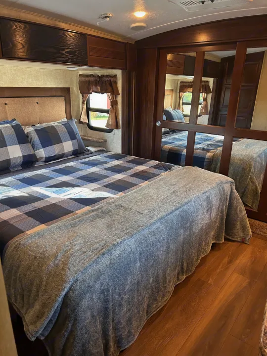 Cozy RV rental bedroom features a comfy bed with blue plaid linens, mirrored closet, and warm wood tones.. Keystone RV Montana Mountaineer 2015