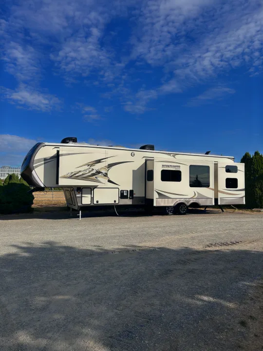 RV rental: Modern fifth-wheel RV parked on a sunny gravel campsite, featuring extended slide-outs.. Keystone RV Montana Mountaineer 2015