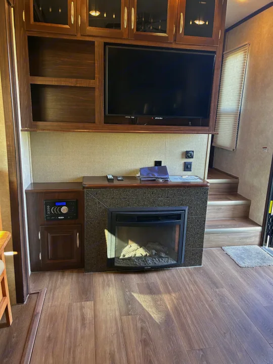 Cozy RV rental living area featuring an electric fireplace, TV, wood floors, and stairs.. Keystone RV Montana Mountaineer 2015