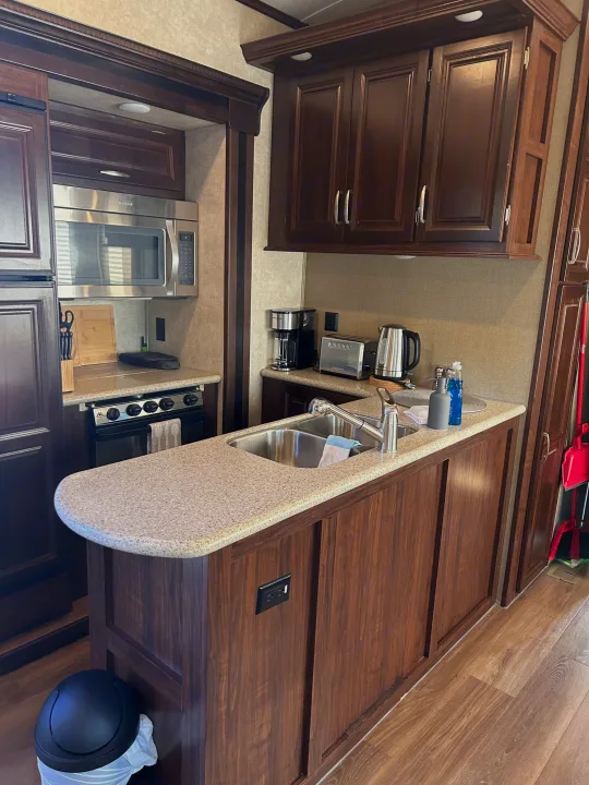 Modern kitchen in an rv rental, showcasing stainless steel appliances like microwave, stove, sink, and well-equipped counter.. Keystone RV Montana Mountaineer 2015