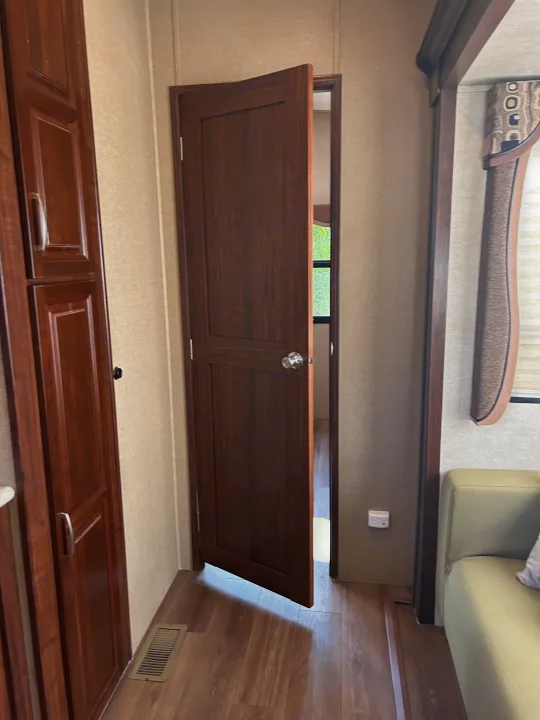 RV rental interior shows dark wood cabinetry, a partially open door, wood-look floor, and a light green sofa.. Keystone RV Montana Mountaineer 2015