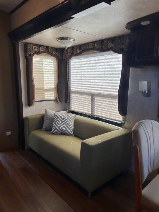Experience comfort in this RV rental's living space: green couch, patterned pillows, windows with blinds, and wood floors.. Keystone RV Montana Mountaineer 2015