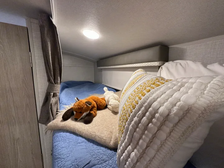 Inside an RV rental: a cozy bunk bed with blue bedding, a fox and rabbit plush, and a decorative pillow.. Forest River Rockwood Geo Pro 2021