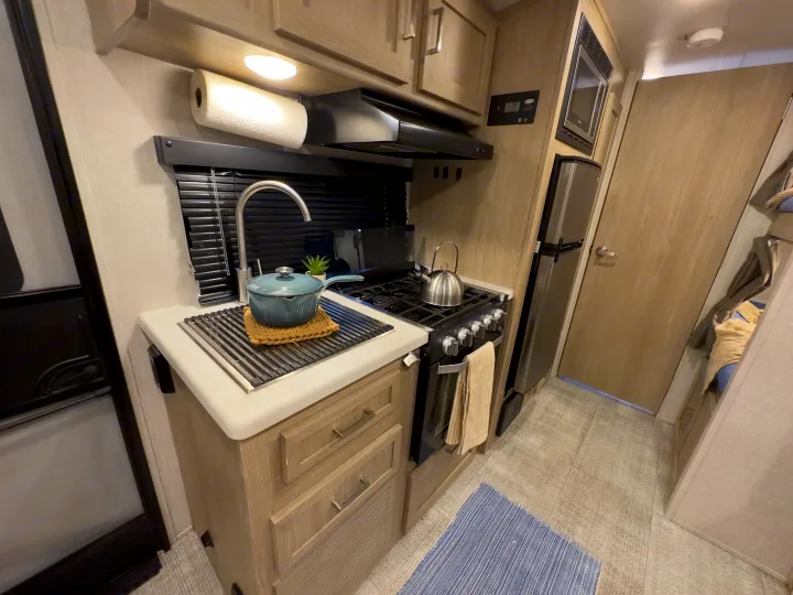 Compact RV rental kitchen: sink with drying rack, stovetop, microwave, and fridge, designed for convenient travel.. Forest River Rockwood Geo Pro 2021