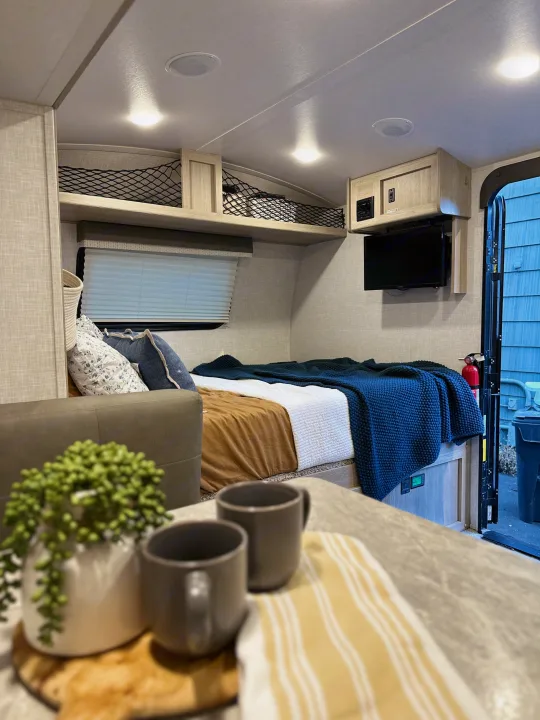 Inside a modern RV rental: a cozy bed with blankets, mounted TV, and netted overhead storage for compact living.. Forest River Rockwood Geo Pro 2021