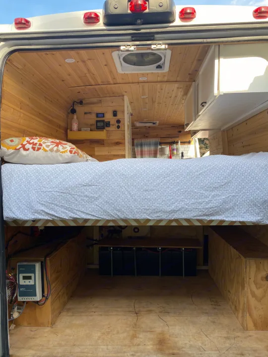 RV rental: Camper van interior from the back, revealing a comfortable bed, wood-paneled walls, under-bed power system & storage.. Other Other 2015