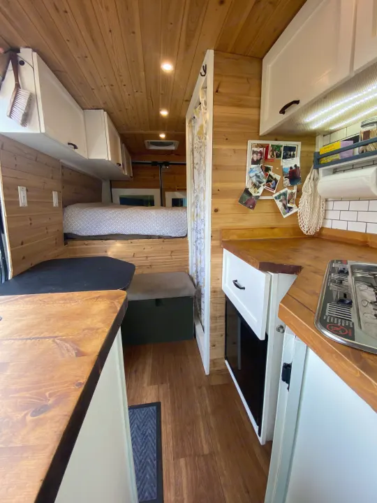Warm wood interior of an RV rental, featuring a cozy kitchen with stove, bed, and inviting living space.. Other Other 2015