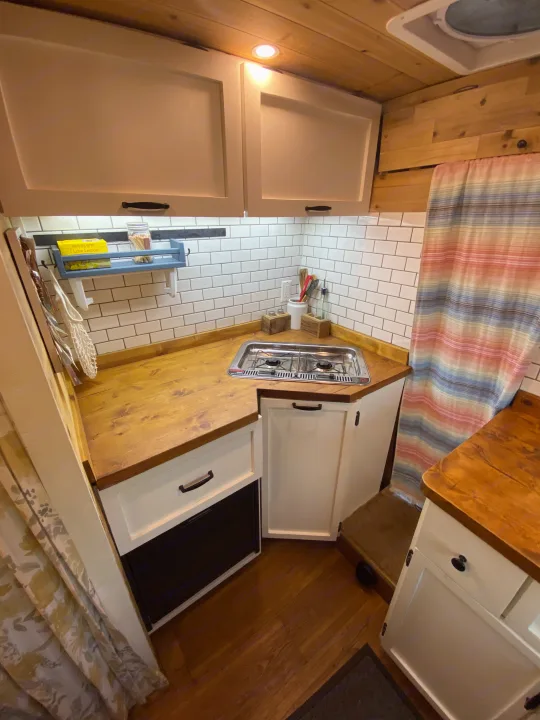 Inside an RV rental: a compact kitchen with warm wood finishes, white subway tiles, two-burner stove, and storage.. Other Other 2015